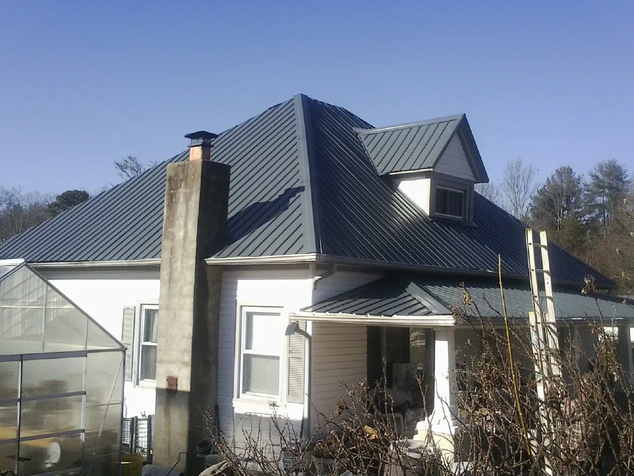 Dark blue standing seam metal roof on a white farmhouse with dormer — Slate & Tile Roof Repair by Roofing Brothers in Bonner