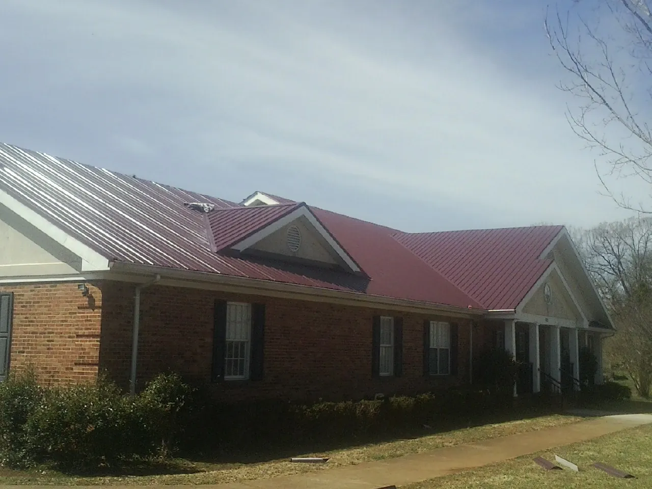 Red metal roof with gabled entries on a long brick building, from a Hail Damage Roof Repair job in Bonner