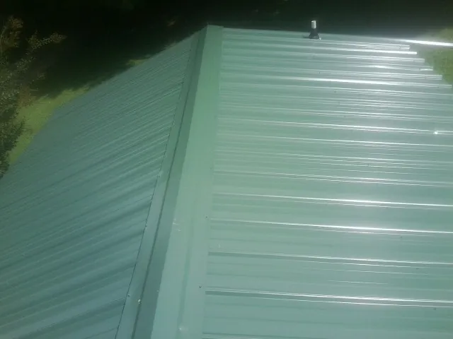 New green metal panels meeting at the ridge of a roof — Flat Roof Repair work by our crew in Bonner