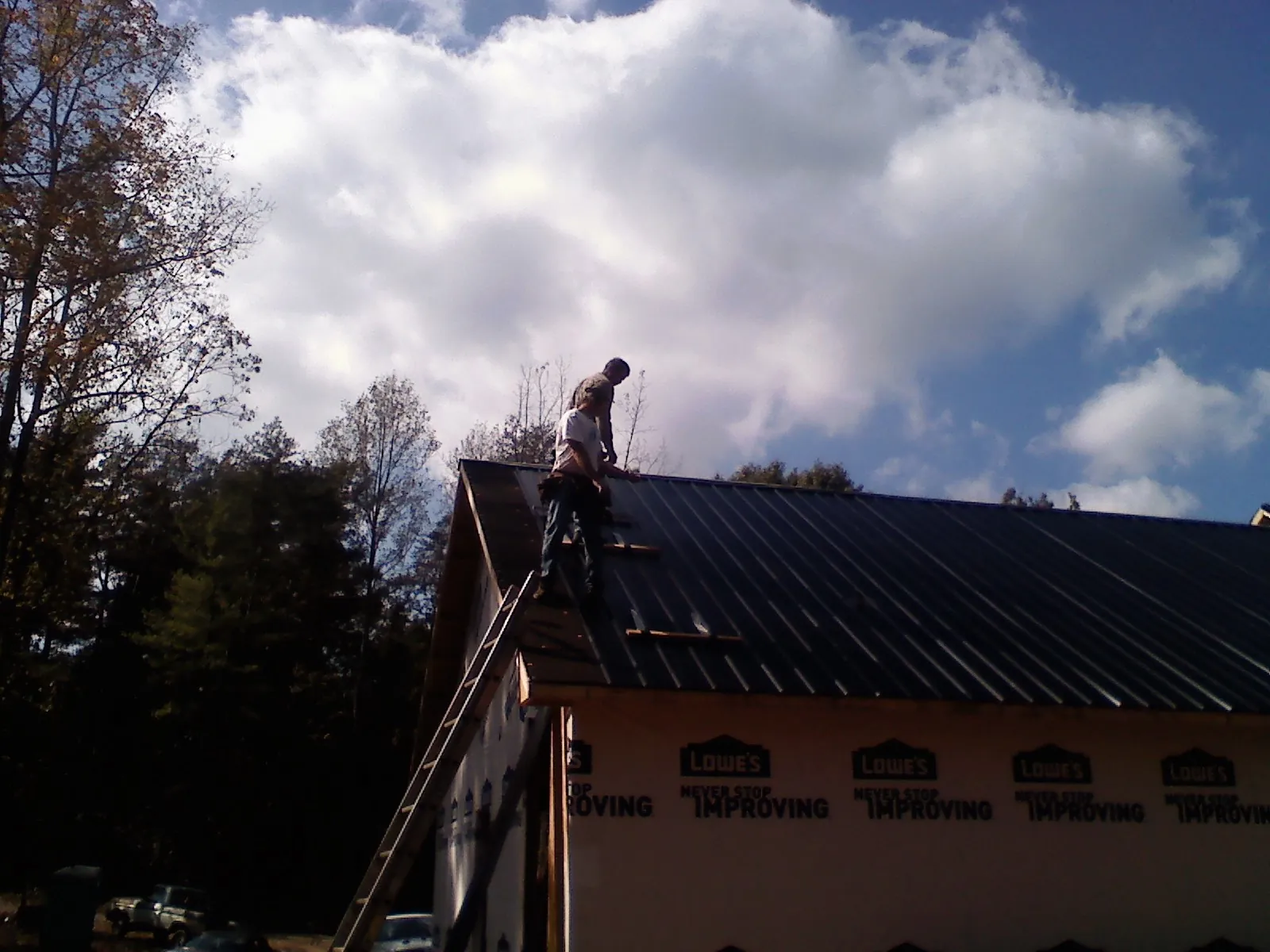 Roofer fastening dark metal panels high against a cloudy sky, from a Roof Inspection job in Bonner