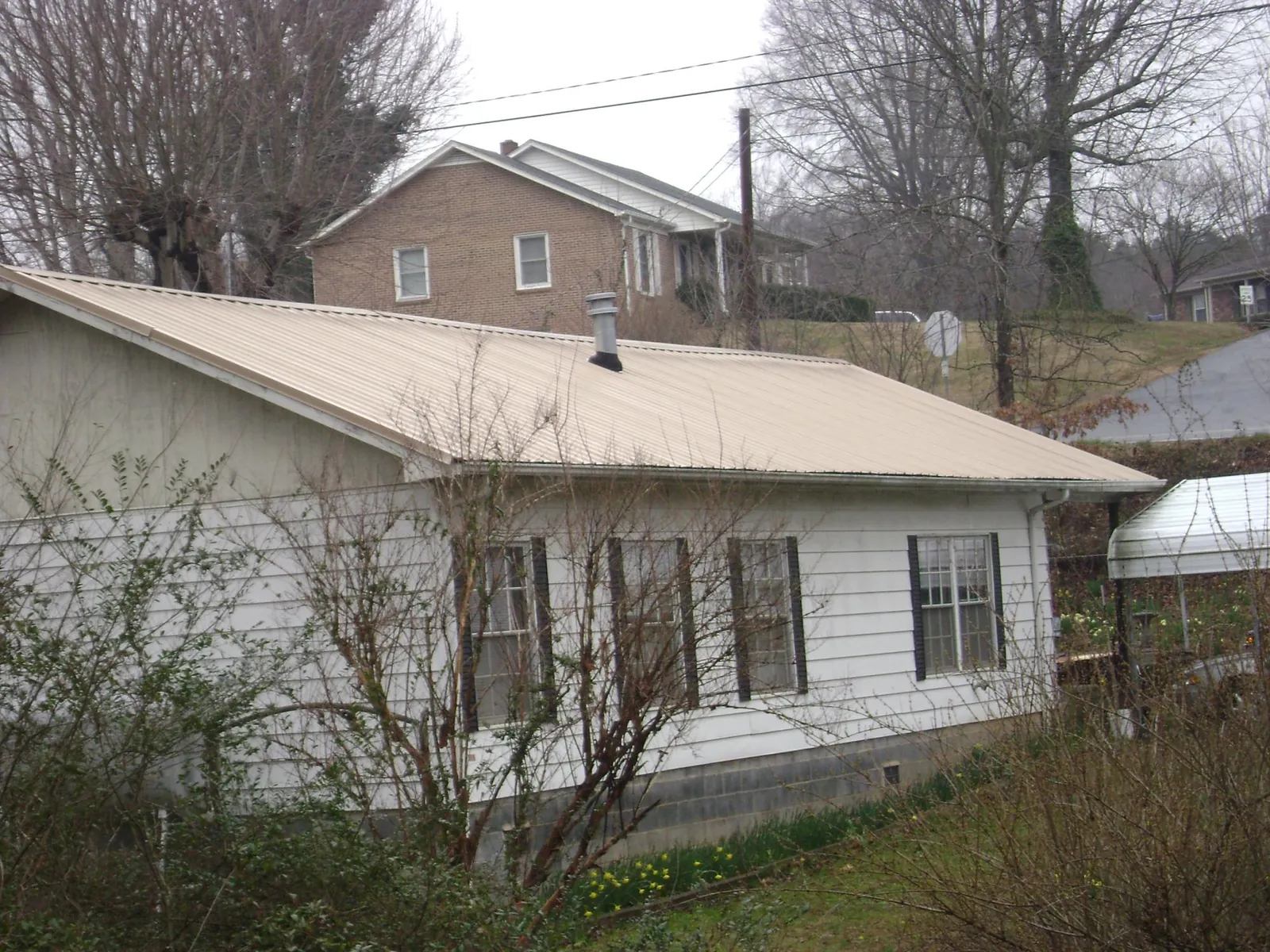Tan metal roof on a white sided house set into a hillside — Commercial Roofing by Roofing Brothers in Bonner