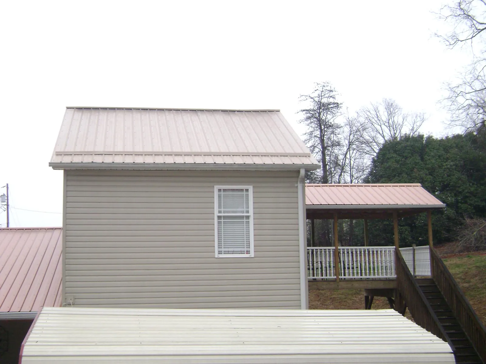 Tan metal roofs on a two story addition and attached porch, from a Roof Replacement job in Bonner